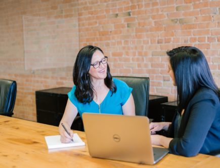 woman in teal t-shirt sitting beside woman in suit jacket