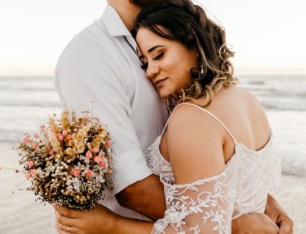 man in white suit kissing woman in white floral dress on beach during daytime
